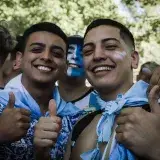 Happy Argentine football fans celebrating outdoors with painted faces and team colors.