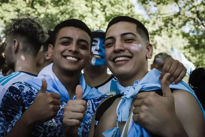 Happy Argentine football fans celebrating outdoors with painted faces and team colors.