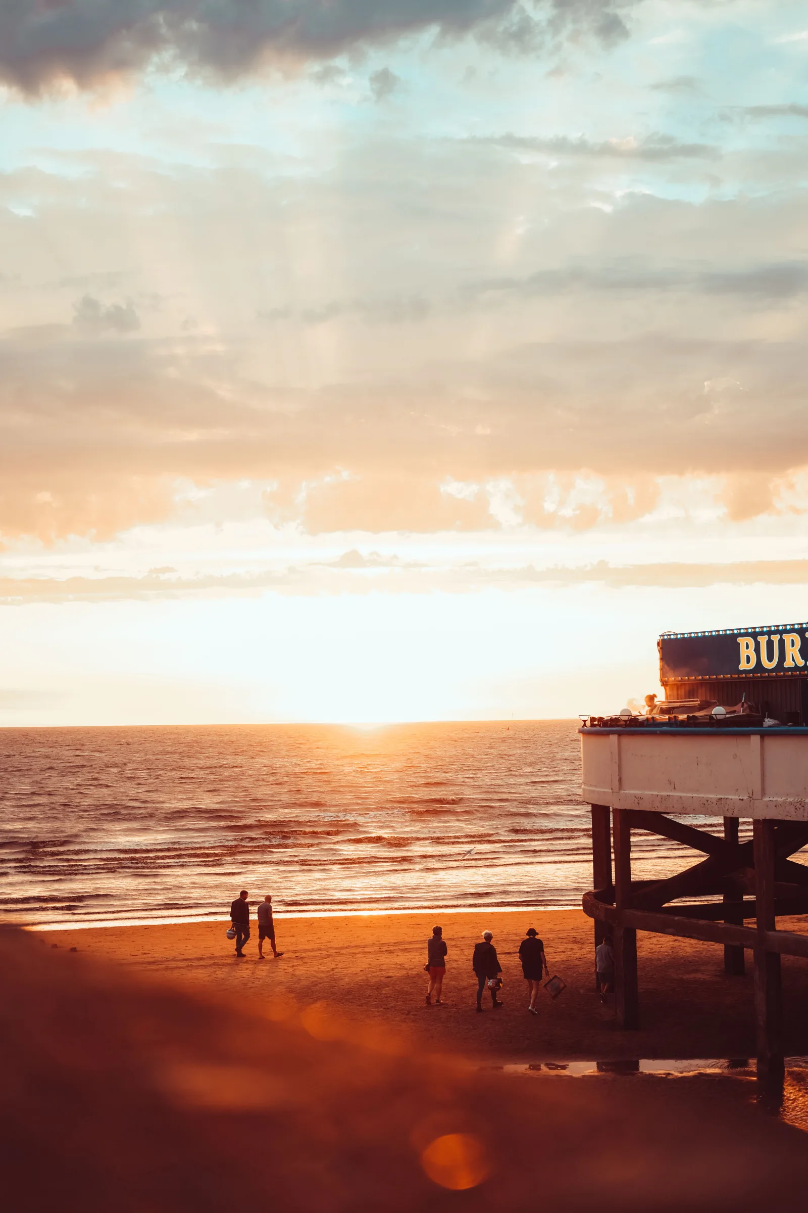 A beautiful sunset over Burnham-on-Sea beach with people walking on the shore.