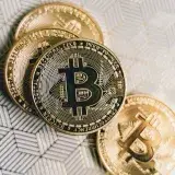 A close-up image of gold Bitcoin cryptocurrency coins on a geometric patterned surface.