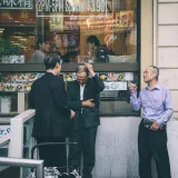Three men interacting outside a Chinatown restaurant in Toronto, capturing urban street life.