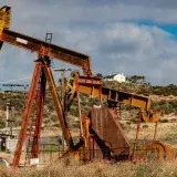 A rusty oil pumpjack situated in a desert-like landscape under a partly cloudy sky.