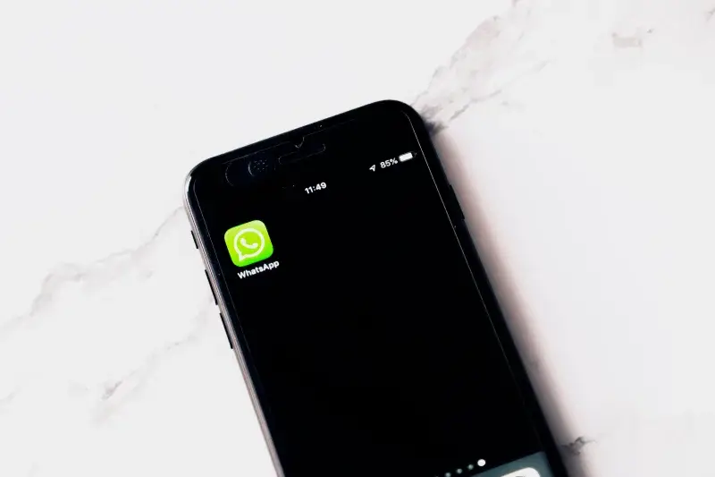 Close-up image of a smartphone displaying WhatsApp on a white table.