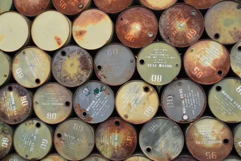 Pile of old, rusty oil barrels stacked outdoors with visible labels and numbers.