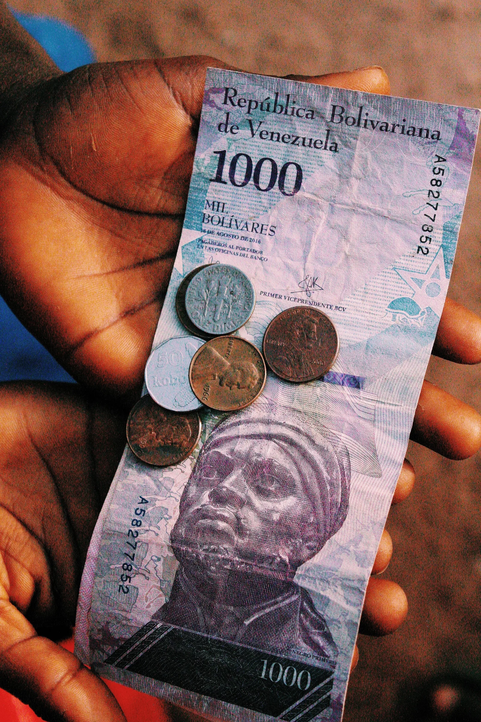 Close-up of hands holding a 1000 Bolivar banknote with coins, capturing the essence of Venezuelan currency.