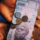 Close-up of hands holding a 1000 Bolivar banknote with coins, capturing the essence of Venezuelan currency.