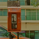 A red payphone on a street in Zacatecas, Mexico against an urban backdrop.