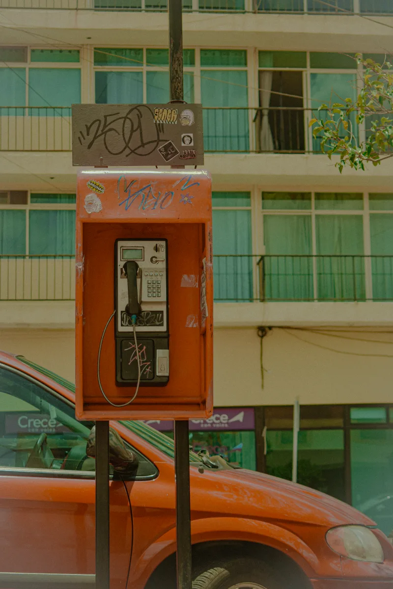 A red payphone on a street in Zacatecas, Mexico against an urban backdrop.