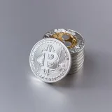 Close-up of shiny Bitcoin cryptocurrency coins with a reflective surface on a gray background.