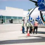 Ground crew in reflective vests preparing an airplane for departure at a sunny airport.