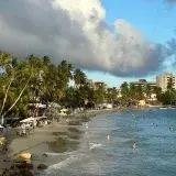 A vibrant beach scene at Pampatar, Venezuela, with palm trees and people enjoying the sunset.