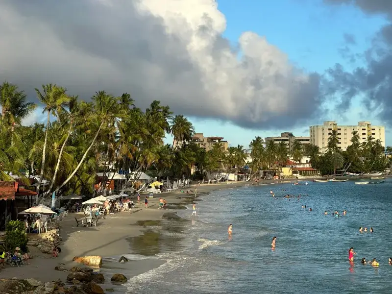 A vibrant beach scene at Pampatar, Venezuela, with palm trees and people enjoying the sunset.