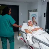 A caring nurse assists a patient in a hospital corridor with a joyful demeanor.