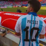 Fan in Argentina jersey with 'Messi 10' watching football match at crowded stadium.
