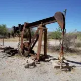 Abandoned rusty oil pumpjack in a barren desert landscape under clear blue skies.