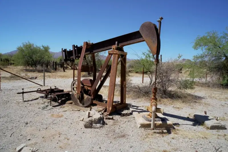 Abandoned rusty oil pumpjack in a barren desert landscape under clear blue skies.