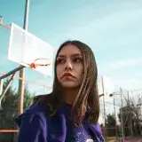 Portrait of a woman in a Lakers hoodie on an outdoor basketball court under a clear sky.