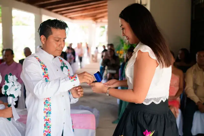 A couple exchanges rings during a vibrant wedding ceremony indoors, surrounded by guests.