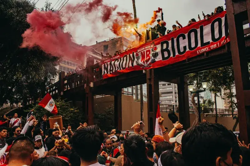 Una escena dinámica de protesta en Lima con una multitud reunida bajo un cielo lleno de humo rojo.