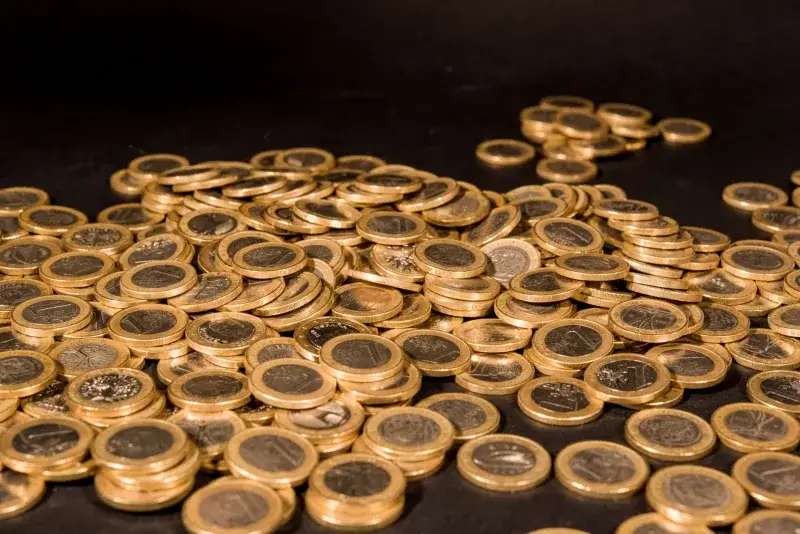 Close-up of a pile of Euro coins scattered on a black surface, representing wealth and finance.
