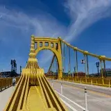A clear daytime view of the Roberto Clemente Bridge in Pittsburgh, showcasing its unique yellow architecture.