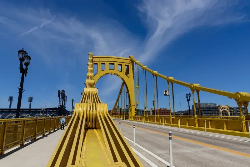 A clear daytime view of the Roberto Clemente Bridge in Pittsburgh, showcasing its unique yellow architecture.