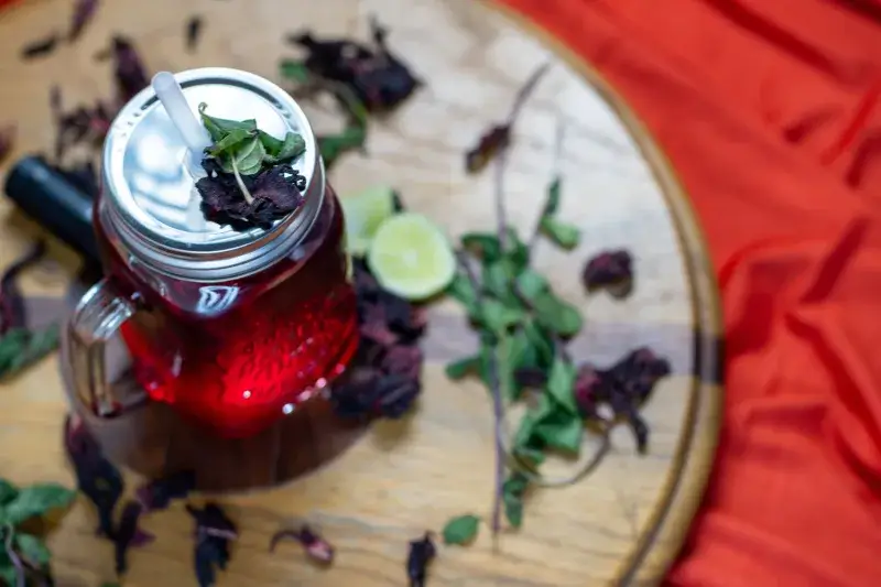 Overhead view of Agua de Jamaica with lime and mint on a wooden surface.