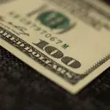 Detailed close-up of a hundred dollar bill resting on dark fabric surface, showcasing texture.
