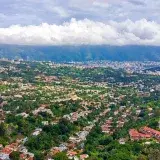 Toma aérea vibrante del paisaje urbano de Caracas con vegetación exuberante y fondo de montaña.