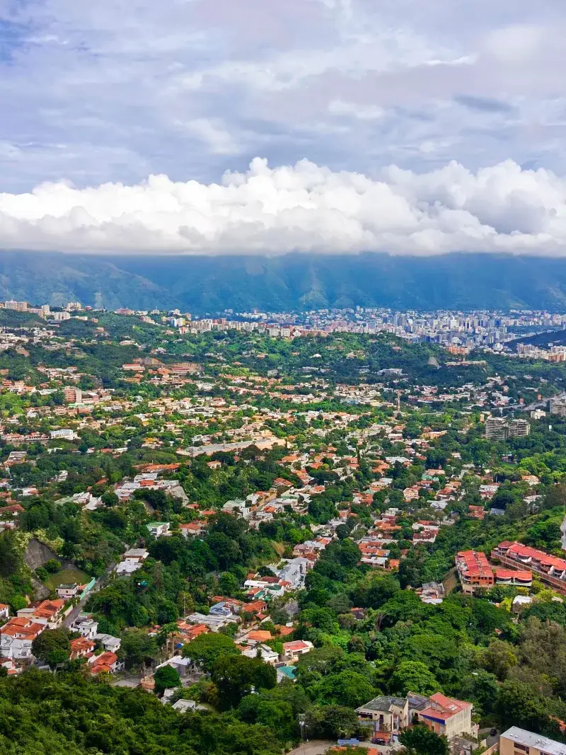 Toma aérea vibrante del paisaje urbano de Caracas con vegetación exuberante y fondo de montaña.