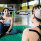 Two women discussing fitness routines indoors, in a lively gym setting.