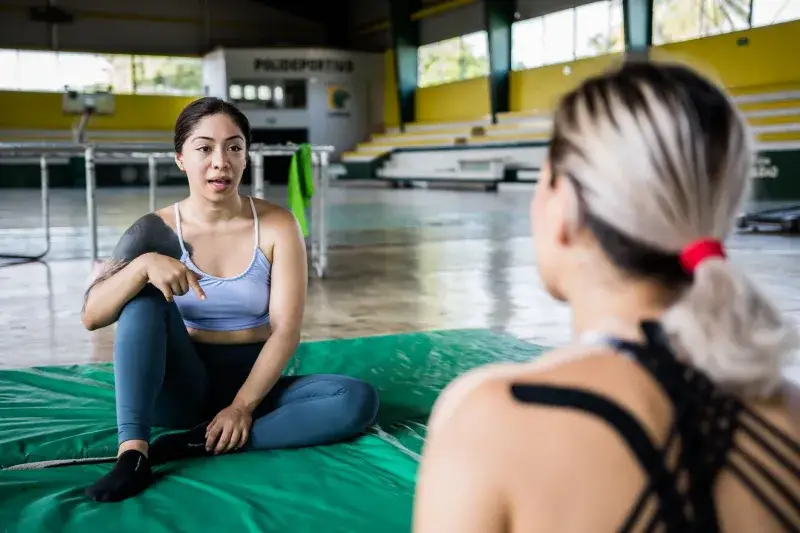 Two women discussing fitness routines indoors, in a lively gym setting.