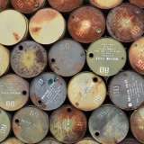 Pile of old, rusty oil barrels stacked outdoors with visible labels and numbers.