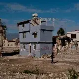 A man walks by a partially demolished house in a devastated urban landscape in Hatay, Türkiye.