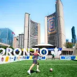 A vibrant soccer scene at Toronto City Hall with players on a sunny day, featuring iconic architecture.