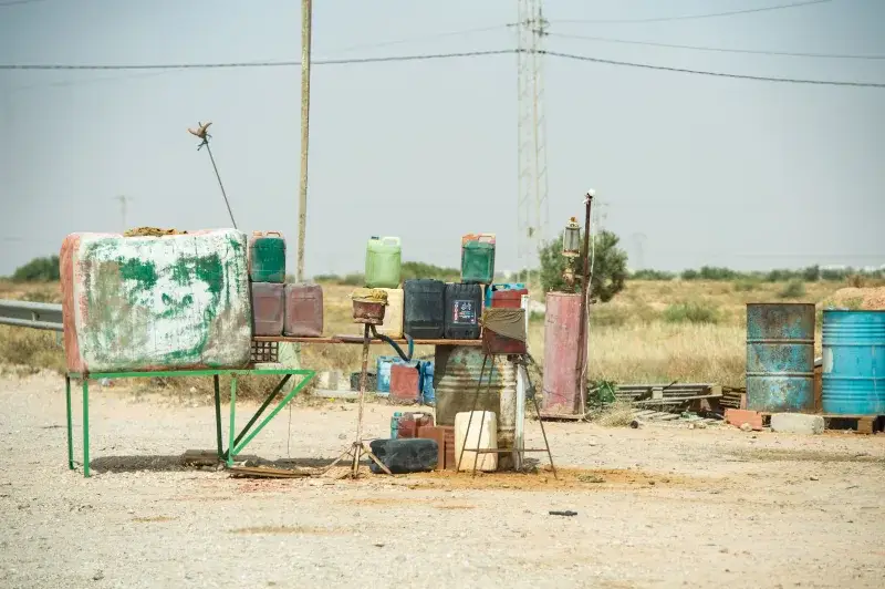 Rustic scene of an abandoned gas station with barrels in the Tunisian desert, showcasing neglect.