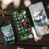 A collection of smartphones showing different app icons, placed on a wooden surface in natural light.