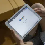 Close-up of hands holding a tablet showing the Google search page.