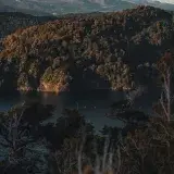 Breathtaking view of a tranquil lake in San Carlos de Bariloche surrounded by lush forests and distant mountains at sunset.