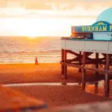 Warm sunset view of Burnham Pier with beachgoers and scenic coastal horizon.