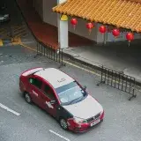 Bird's eye view of a red Proton Saga taxi on a city street adorned with Chinese lanterns.