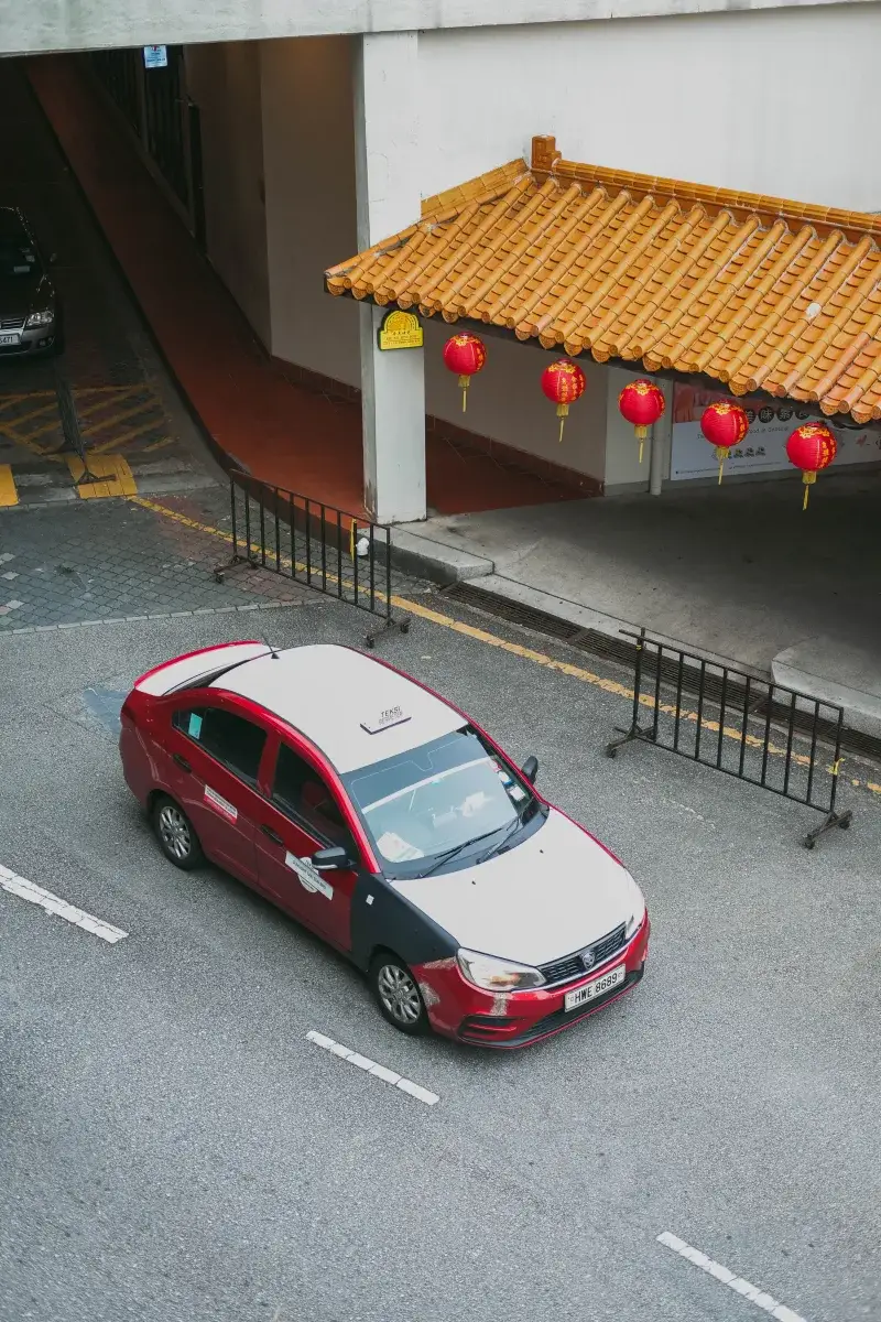 Bird's eye view of a red Proton Saga taxi on a city street adorned with Chinese lanterns.