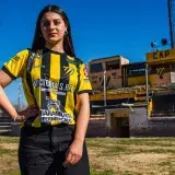 Confident woman posing in a soccer jersey in an outdoor sports field.