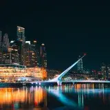 Modern architectural view of Puente de la Mujer and Buenos Aires skyline reflected in water at night.