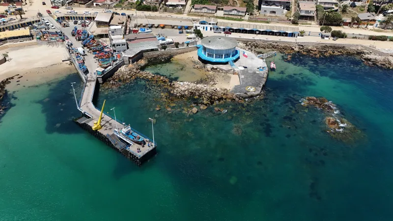 Aerial photograph of Algarrobo pier with fishing boats and coastal buildings, showcasing the vibrant coastal scene in Chile.