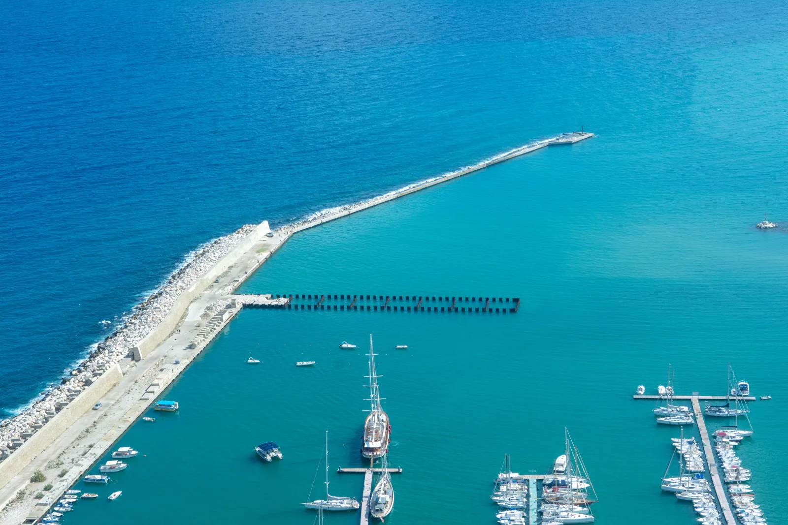Scenic aerial view of Castellammare del Golfo marina with clear blue waters and moored boats in Sicily, Italy.