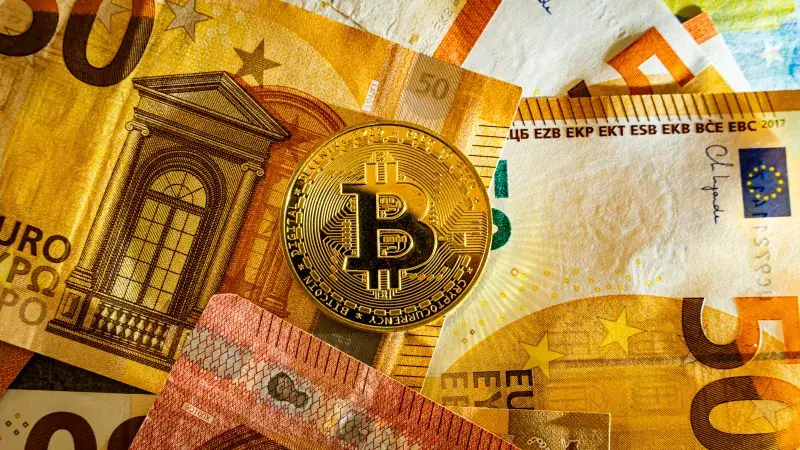 Moneda de Bitcoin dorada colocada sobre billetes de euro, simbolizando la moneda digital y las finanzas modernas.