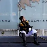 A soldier in traditional military uniform resting against a Malvinas monument in Buenos Aires, Argentina.