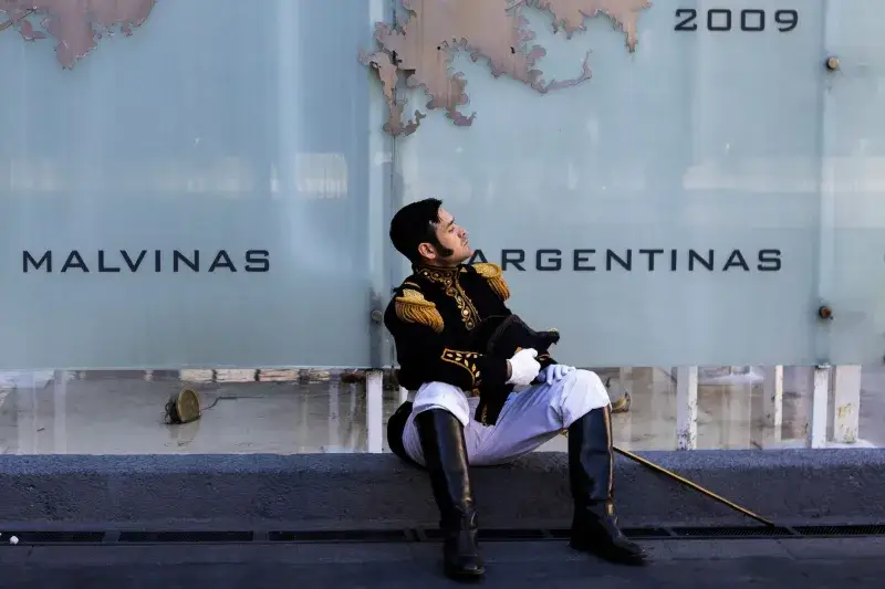 A soldier in traditional military uniform resting against a Malvinas monument in Buenos Aires, Argentina.