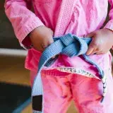 A child in a vibrant pink karate gi confidently tying a blue belt, symbolizing focus and discipline in martial arts.
